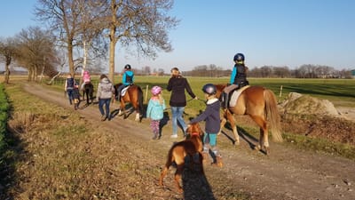 Kinder der Ponyschule beim Ausritt auf einem Feldweg, einige gehen zu Fuß