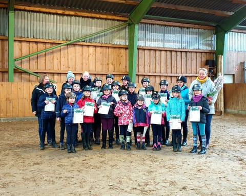 Reitschülerinnen und Reitschüler mit Urkunden nach der Reitabzeichenprüfung in der Reithalle
