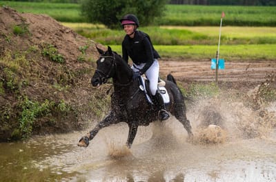 Boomerang galoppiert mit Reiterin spritzend durch einen Wassergraben