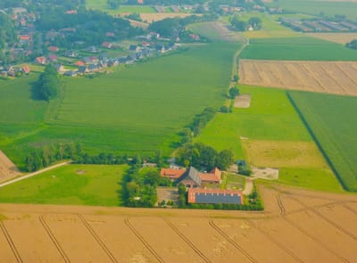 Luftaufnahme des Braaklander Hofs zwischen Feldern und Wiesen, im Hintergrund das Dorf